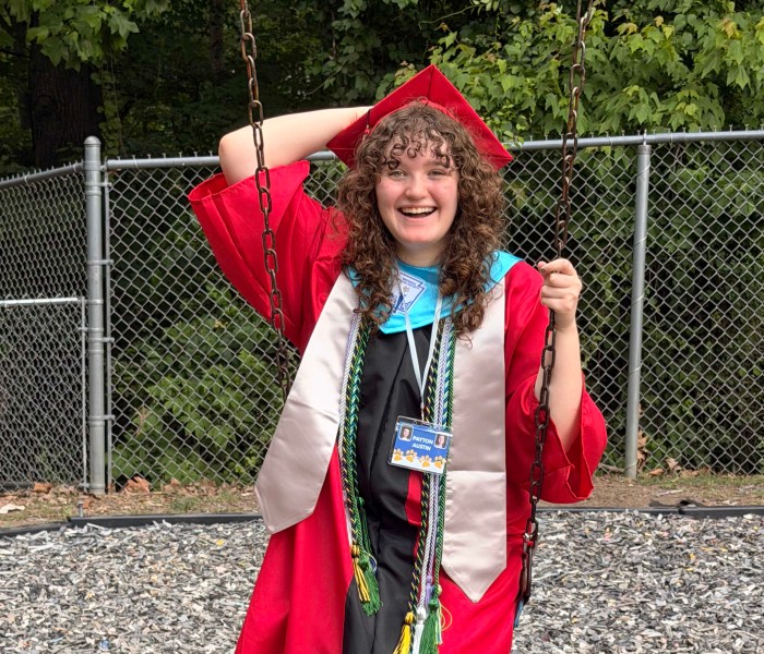Payton wears her red cap and gown while swinging on the playground outside of her high school graduation