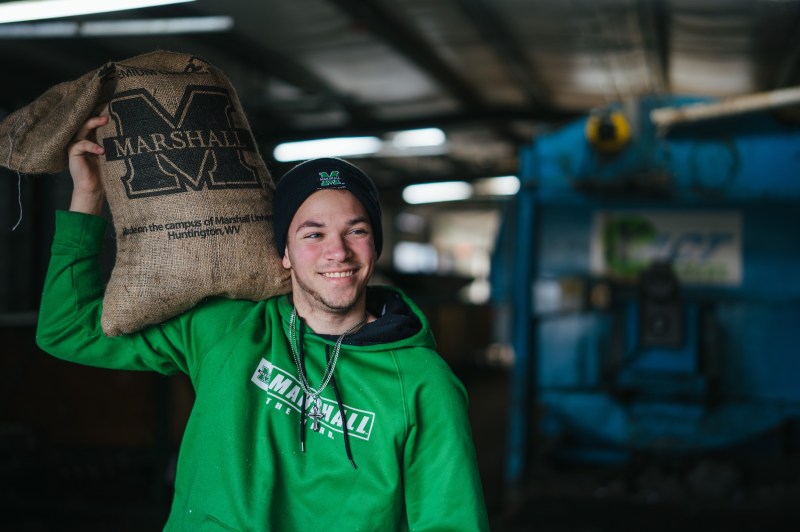 student holding a bag of herd dirt compost with commercial composter in the background