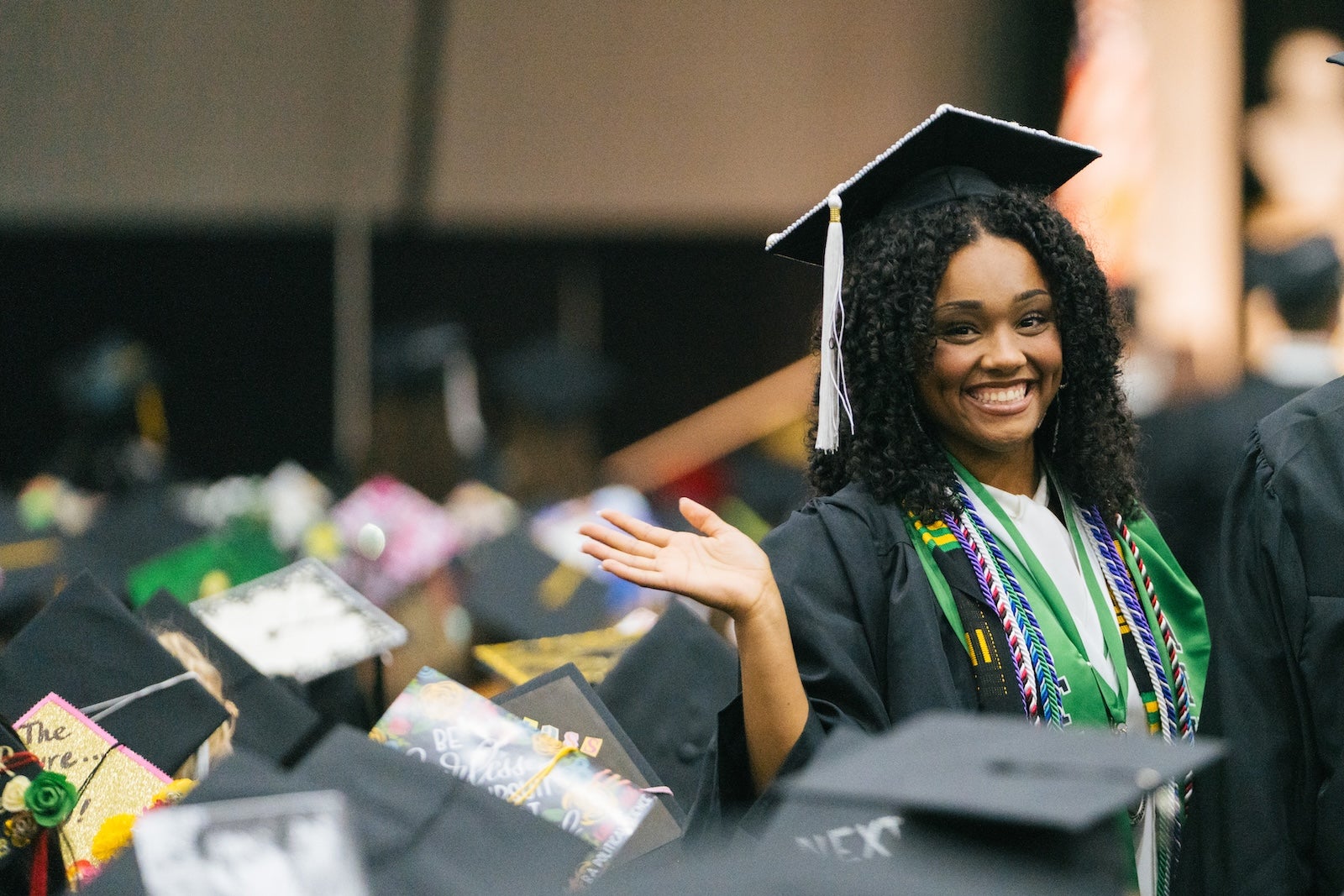 student smiling and waving at commencement
