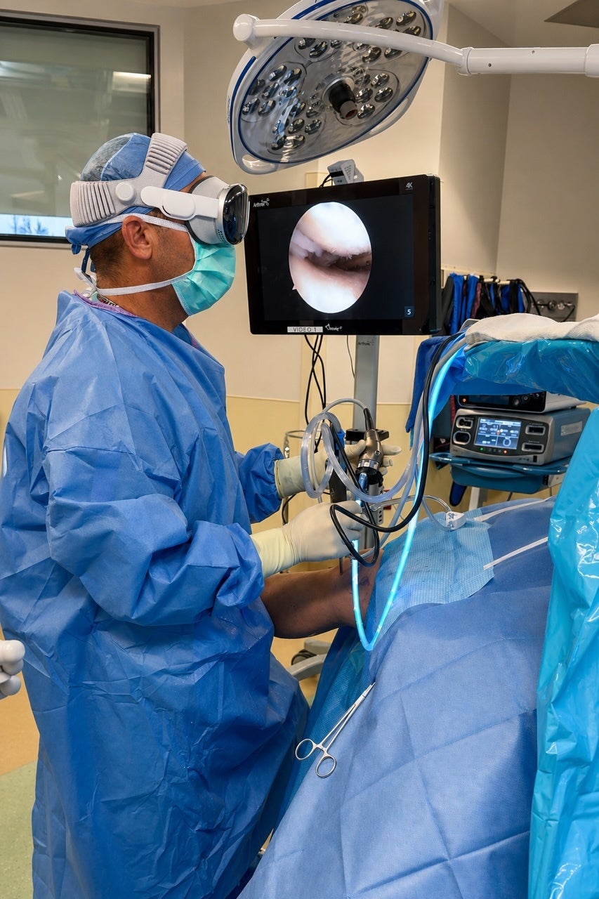 Surgeon in blue scrubs looking at a video monitor.