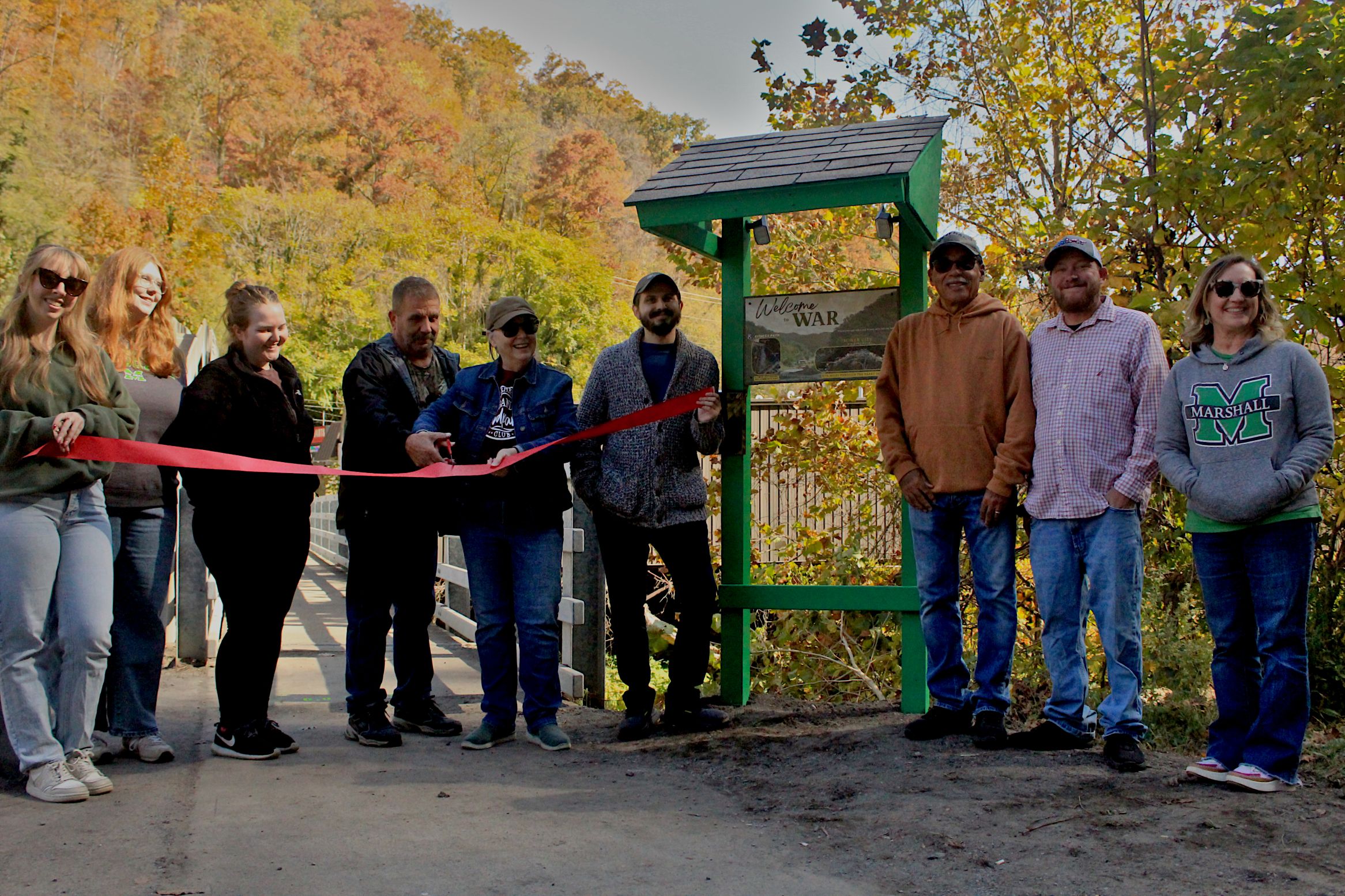People cutting a ribbon on a trail in the fall.