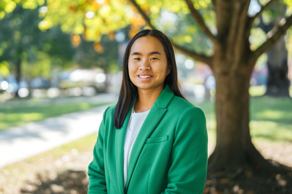Hanna Shrout wears a green blazer and smiles at the camera from the Marshall University campus