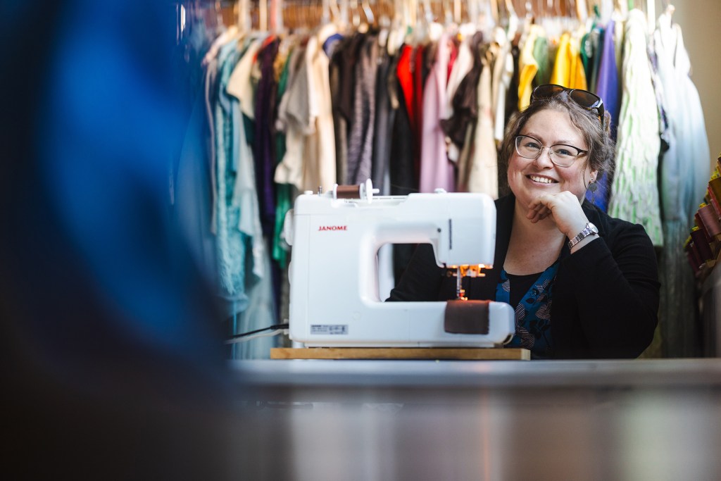 Olivia Trees sits behind her sewing machine and smiles at the camera