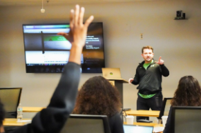 man presents to class, student raises his hand