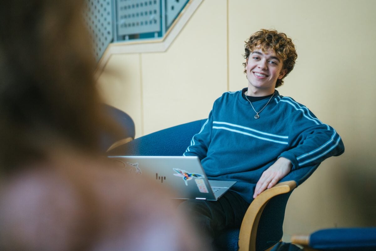 student on a laptop int he library smiling at the camera