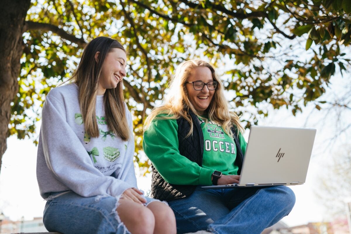 two students outside on a laptop laughing and smiling