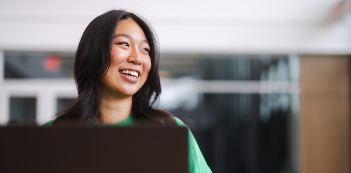 student working on a laptop and smiling to the side