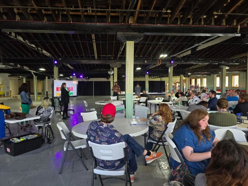 woman presenting to a group of people seated at tables in a warehouse