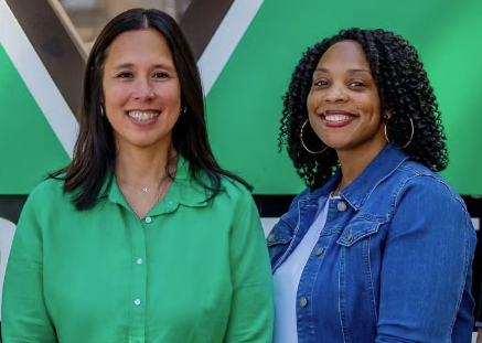 two women smiling in front of green M