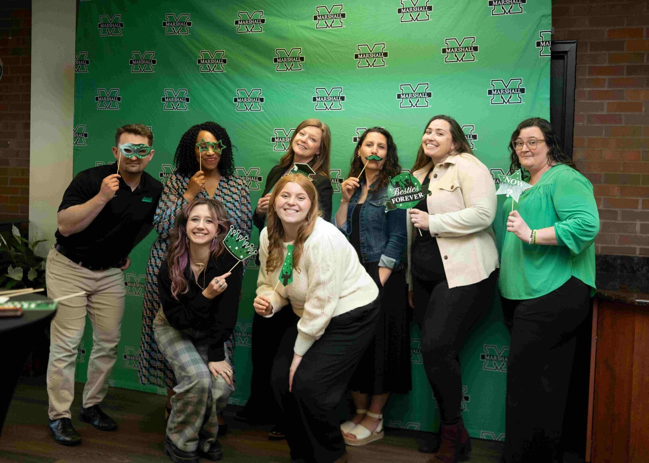 group of people in front of green banner smiling and holding up grad masks
