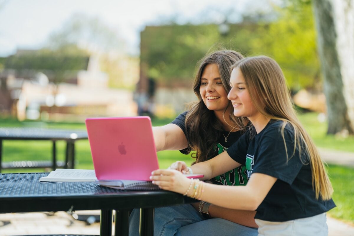 two students looking at a laptop and smiling outside