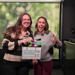 Two smiling women hold a film slate reading 