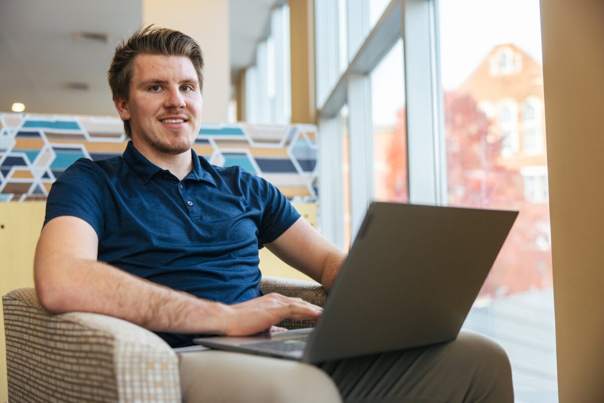 student working on a laptop in the library and smiling at the camera