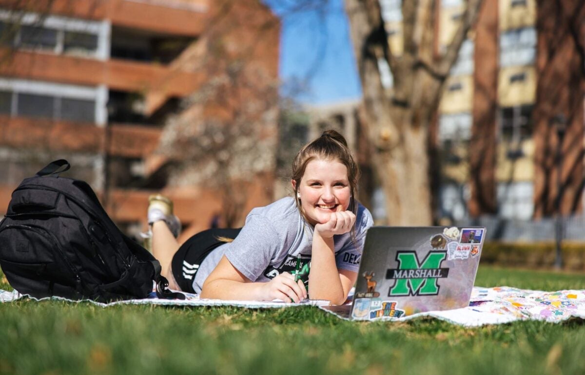 student working on a laptop laying on a blanket