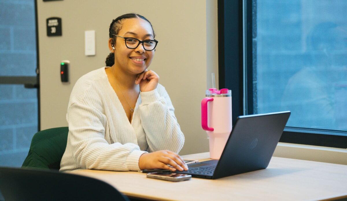 student working on a laptop and smiling at the camera