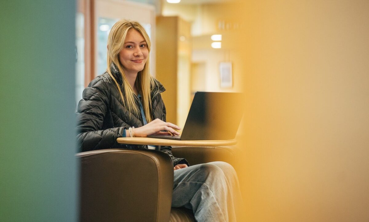 student working on a laptop in the library and smiling at the camera