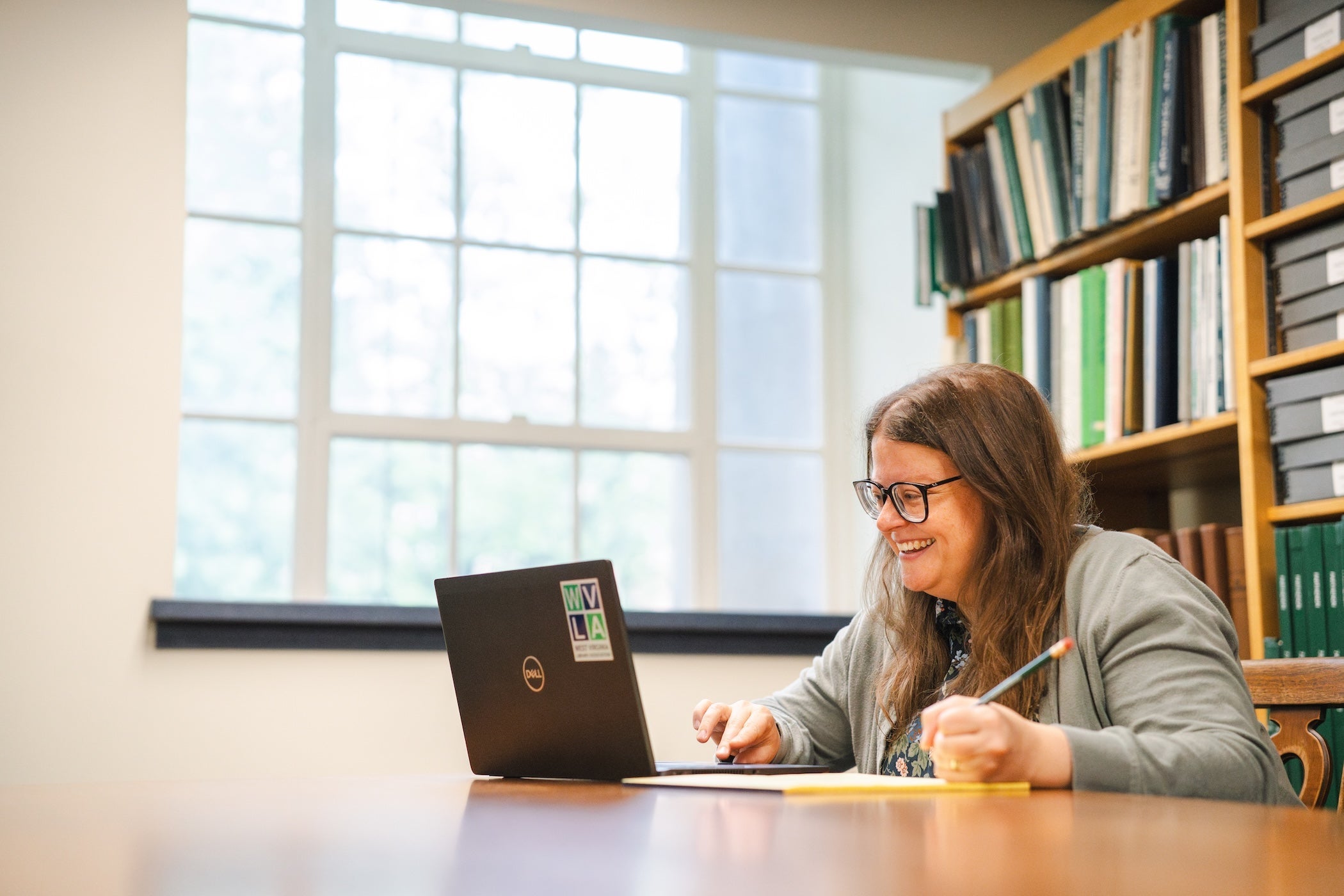 faculty member working on a laptop in the library and taking notes