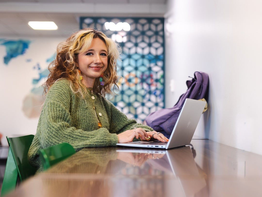 A student looks at the camera while working on a computer