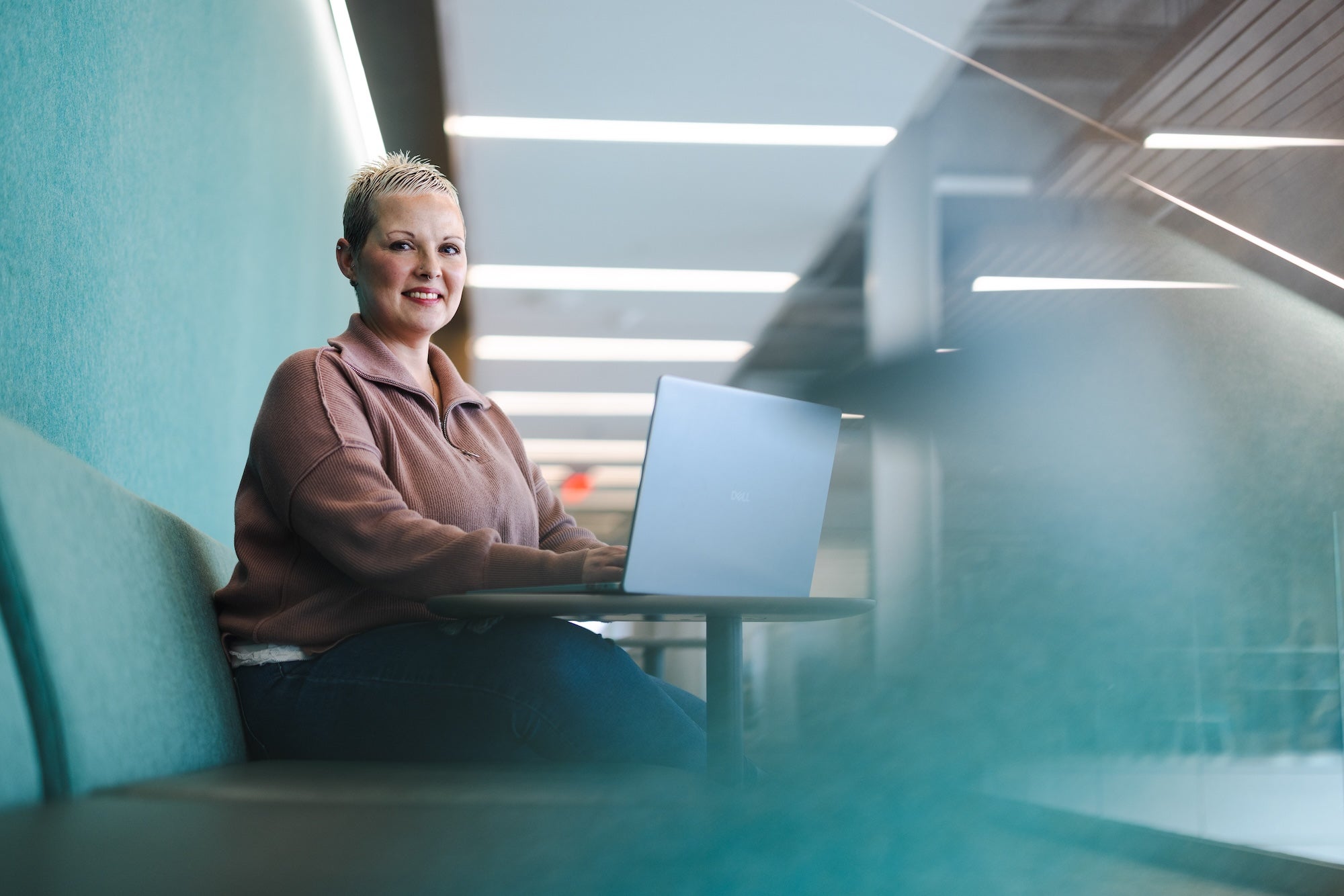 student working on a laptop in the school of business and smiling at the camera