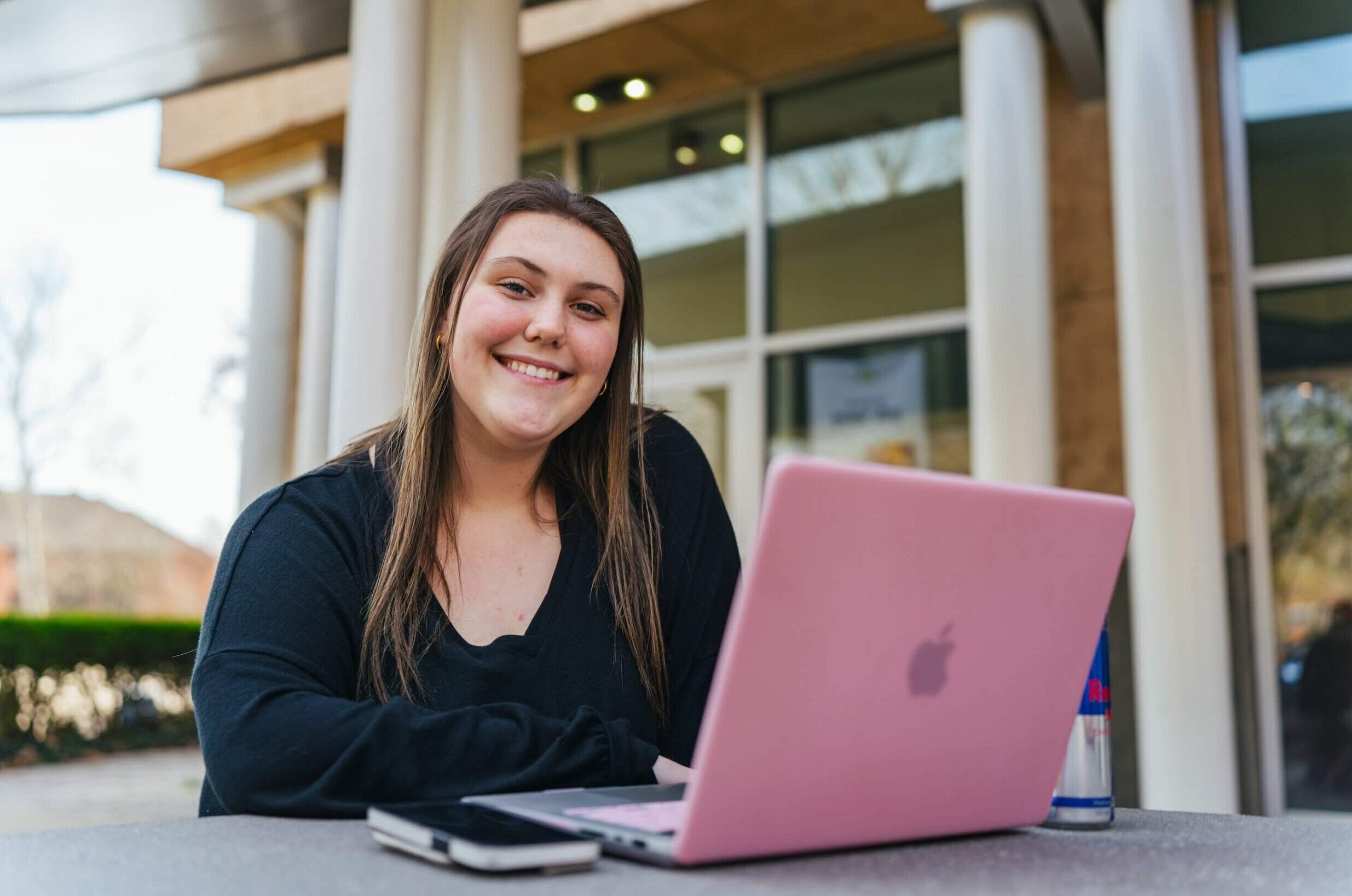 student working outside on a laptop and smiling at the camera