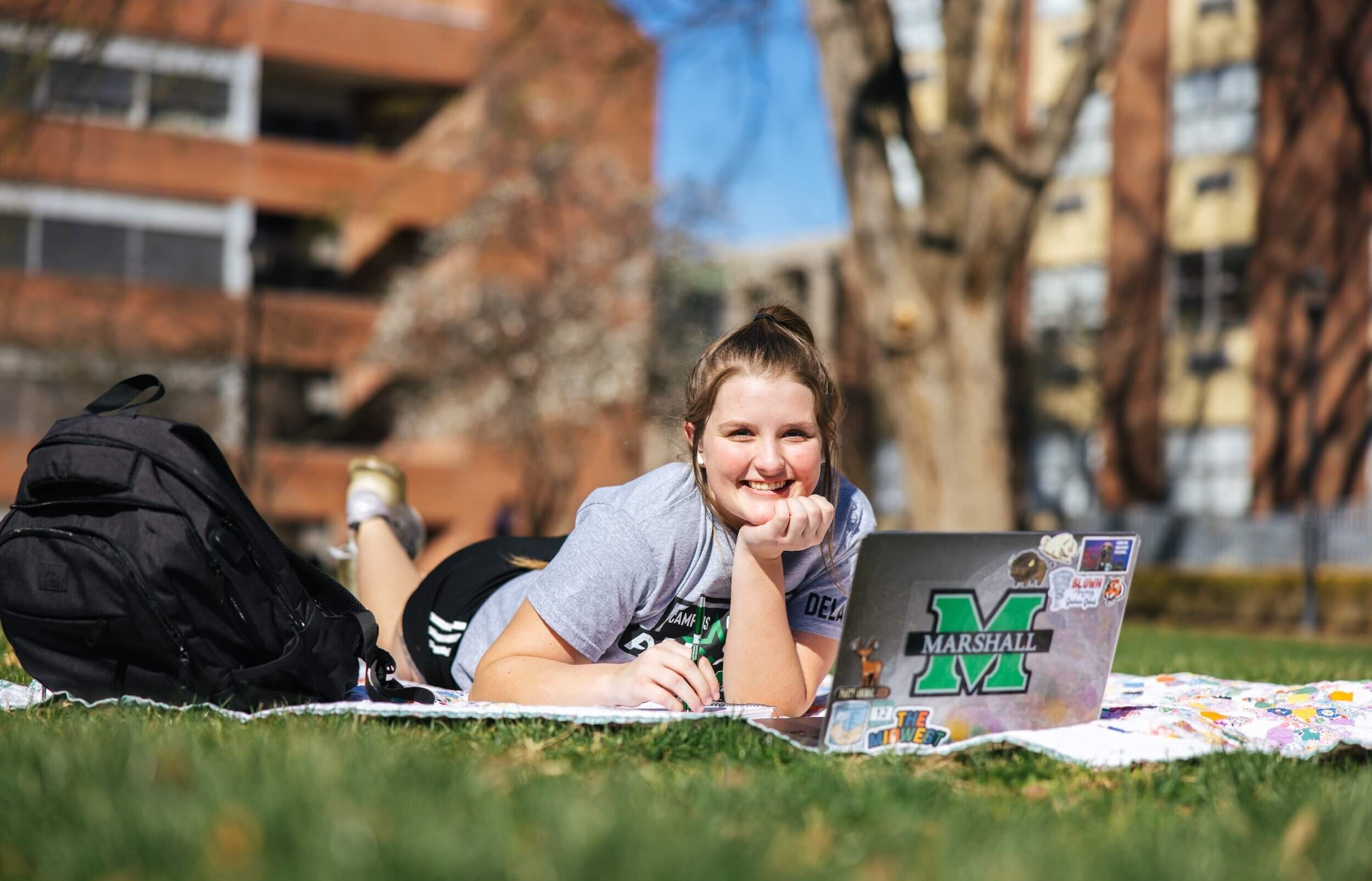 student working on a laptop laying on a blanket