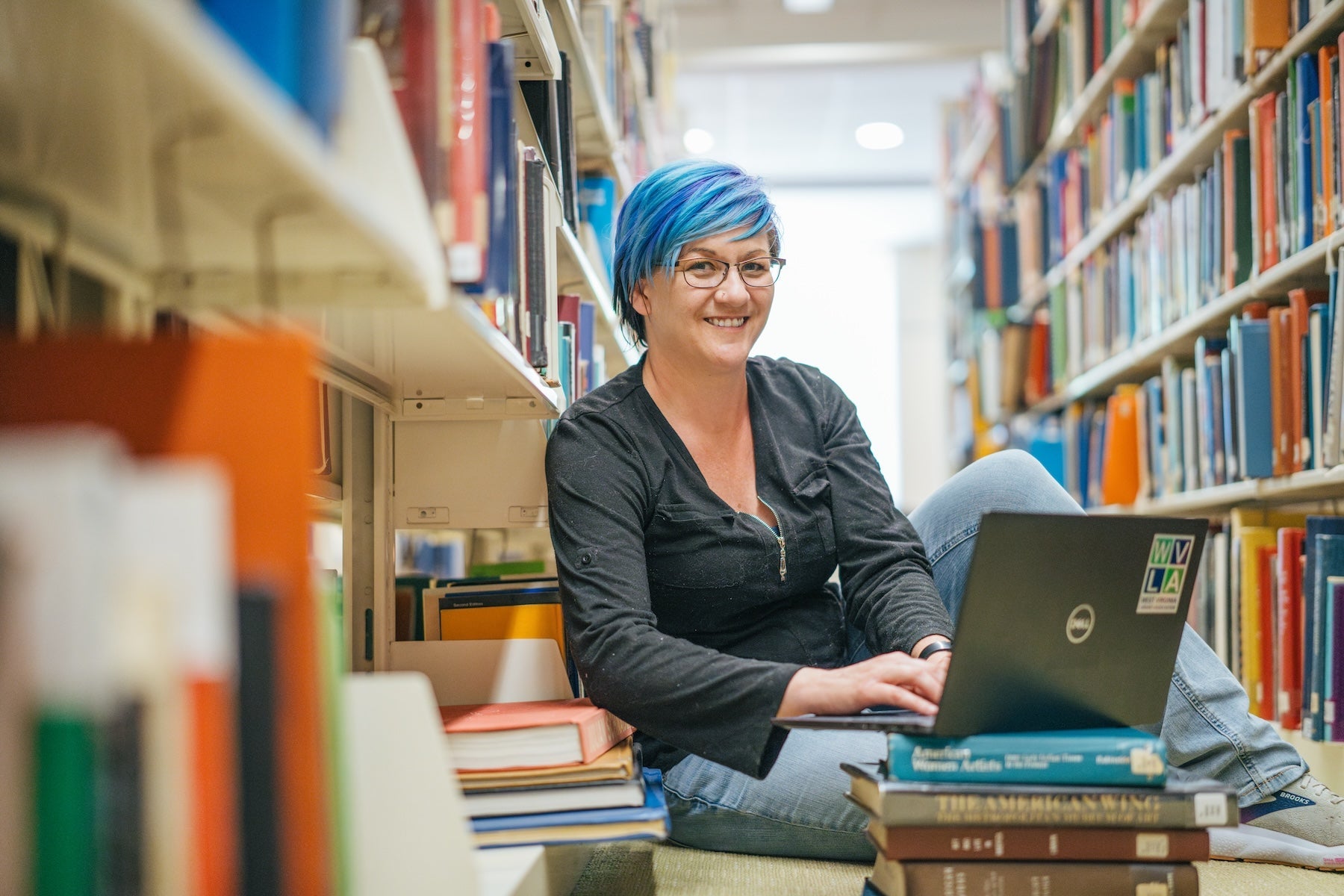 student in the library in between shelves of books working on a laptop