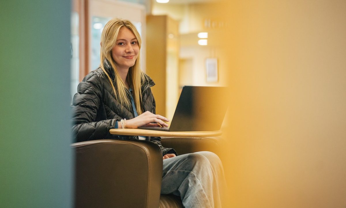 student working on a laptop in the library and smiling at the camera