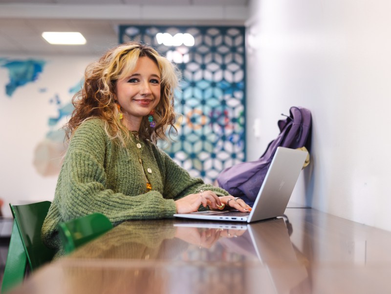 A student looks at the camera while working on a computer