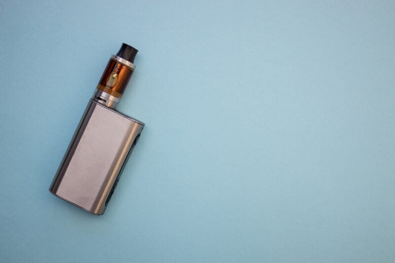 Vape pen metal electronic cigarette with vaping blue background top view