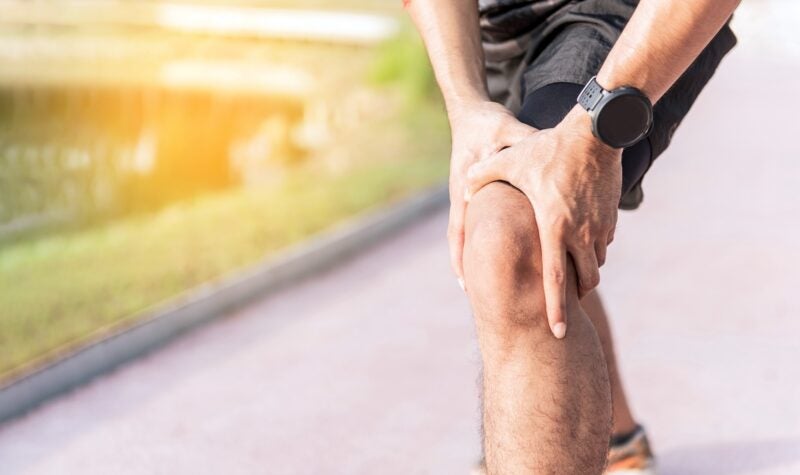 Injury from workout concept : The man use hands hold on his knee while running on road in the park. Shot in morning time