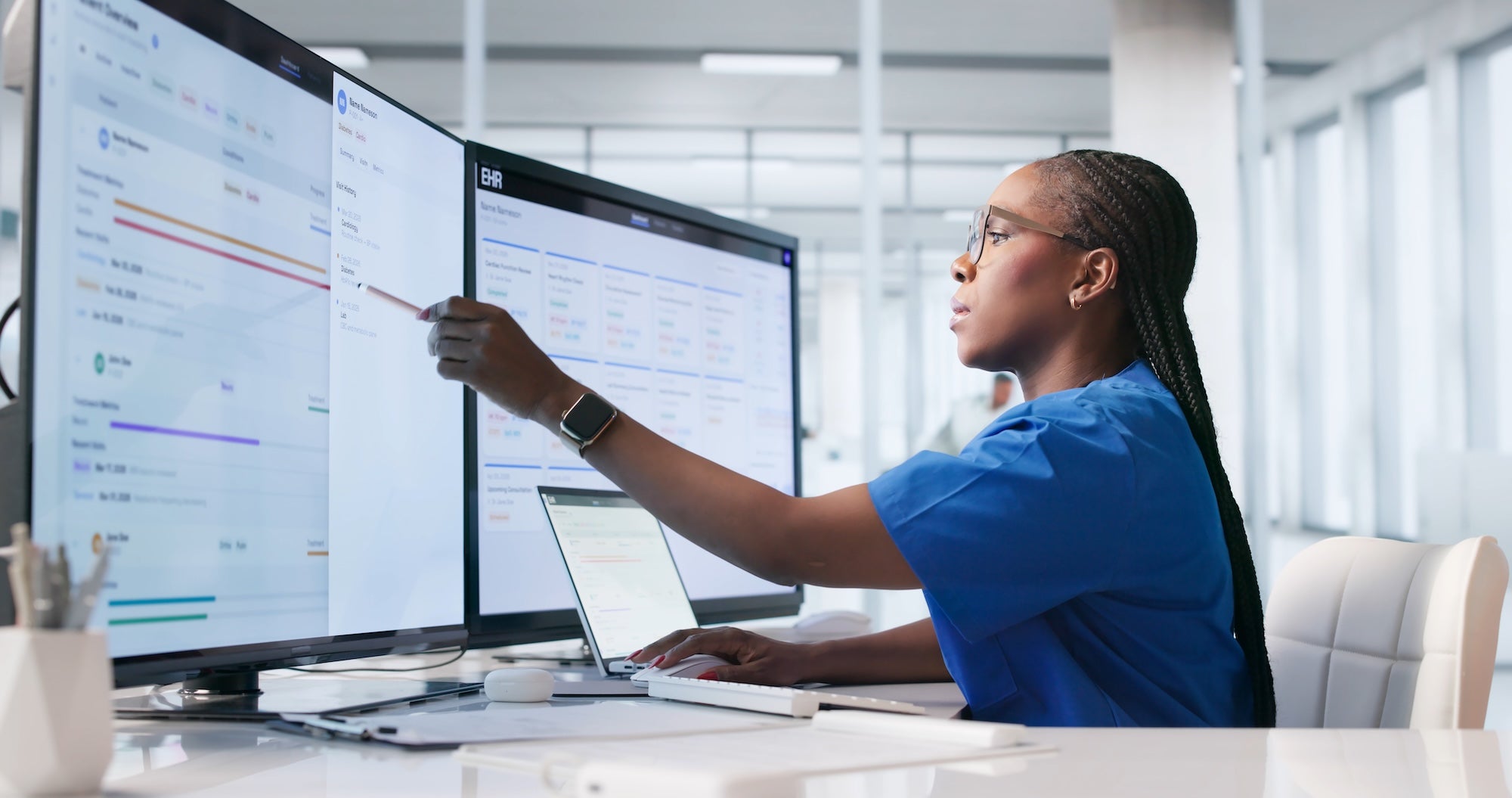 Young Female Healthcare Worker Reviews Patient Records On Laptop In Hospital.