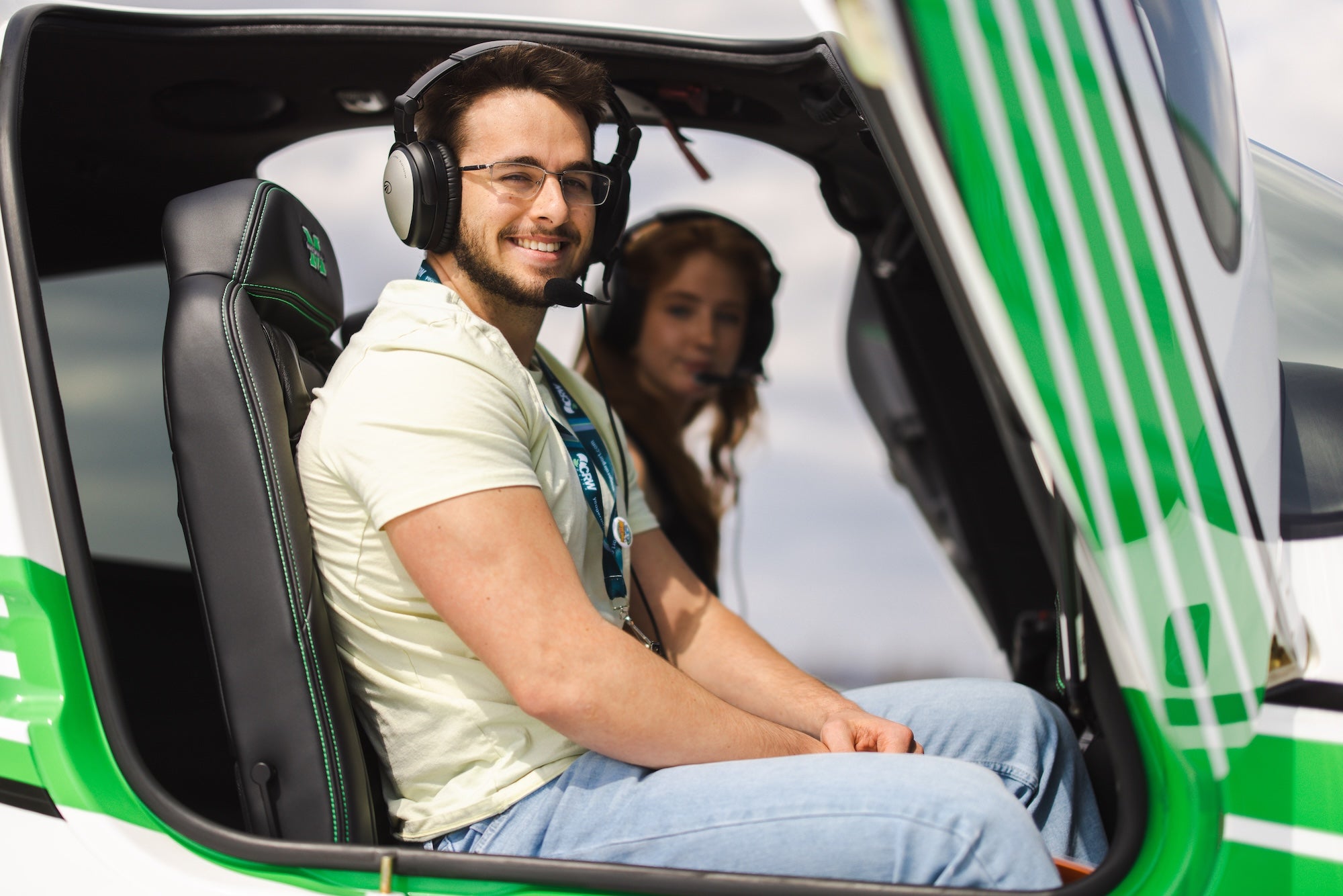 two students sitting in a Marshall plane with headsets on and smiling at the camera