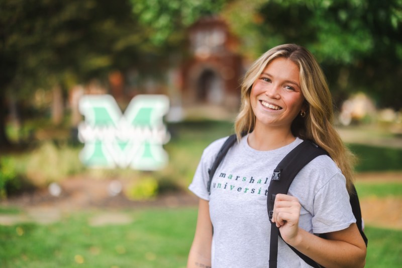 student wearing a backpack and smiling in front of the block M on campus
