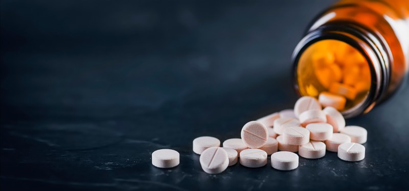White medical pills or tablets with bottle on black background. Macro side view with copy space.