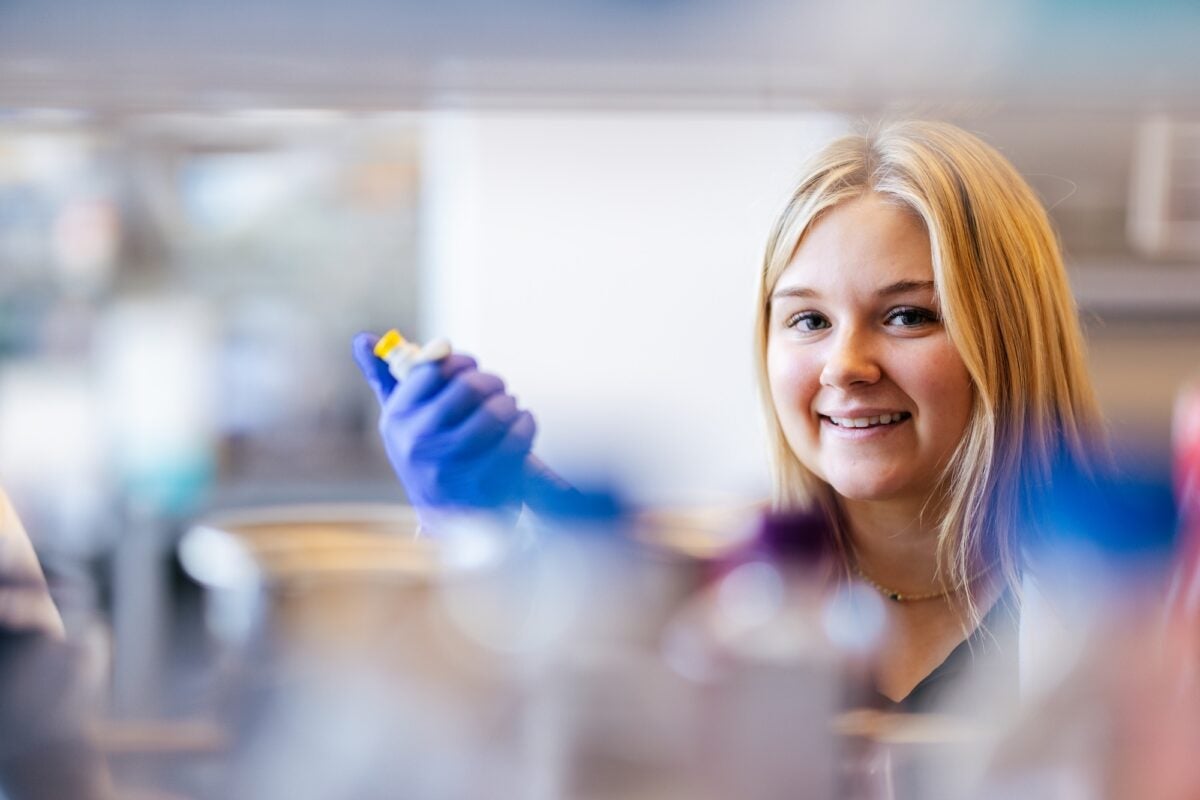 Student wearing protective gloves uses a pipette during a laboratory experiment.