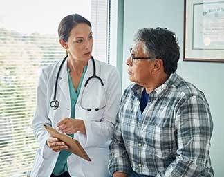 Medical consultation showing a physician speaking with a seated patient in an exam room