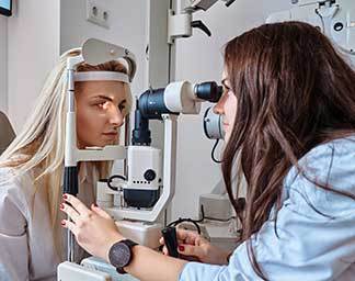 Eye examination showing an optometry patient positioned at a slit lamp microscope while an optometry professional adjusts the instrument to evaluate eye health and vision