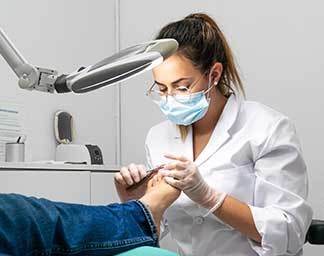 Clinical exam showing a podiatric professional carefully examining a patient’s foot under a task light, focusing on nail and skin health