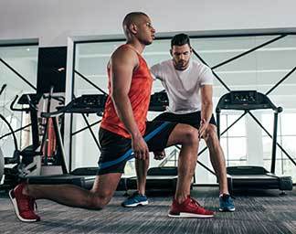 Athletic training session showing a trainer guiding an individual through a resisted lunge exercise using a resistance band to improve lower body strength and stability