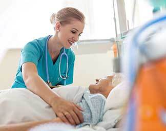 Nursing care setting showing a nurse adjusting a patient’s blanket while the patient rests in a hospital bed, with medical equipment nearby