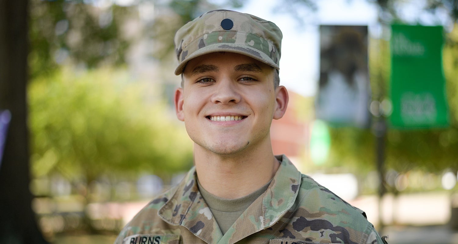 A Marshall University ROTC student stands smiling while wearing his uniform on campus