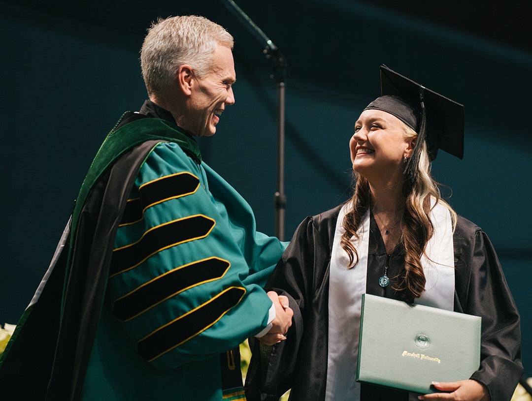 A Marshall University graduate shakes hands with President Brad D. Smith during a commencement ceremony