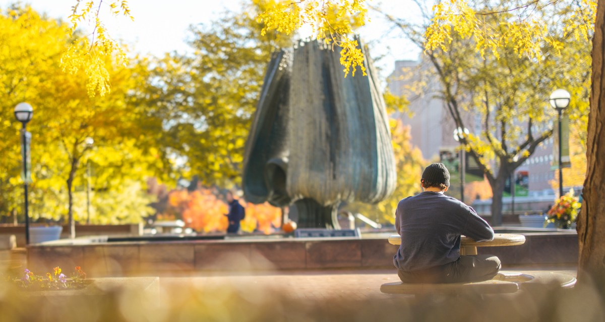 A student sits at a table in front of the Memorial Fountain on the Marshall University Plaza