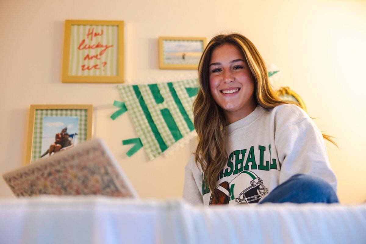 student working on a laptop in a residence hall and smiling at the camera
