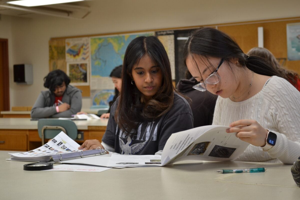 two students looking at a packet of papers at a desk