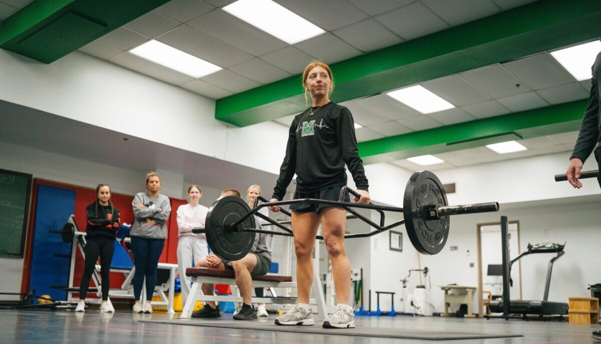 student lifting a weight bar in a gym