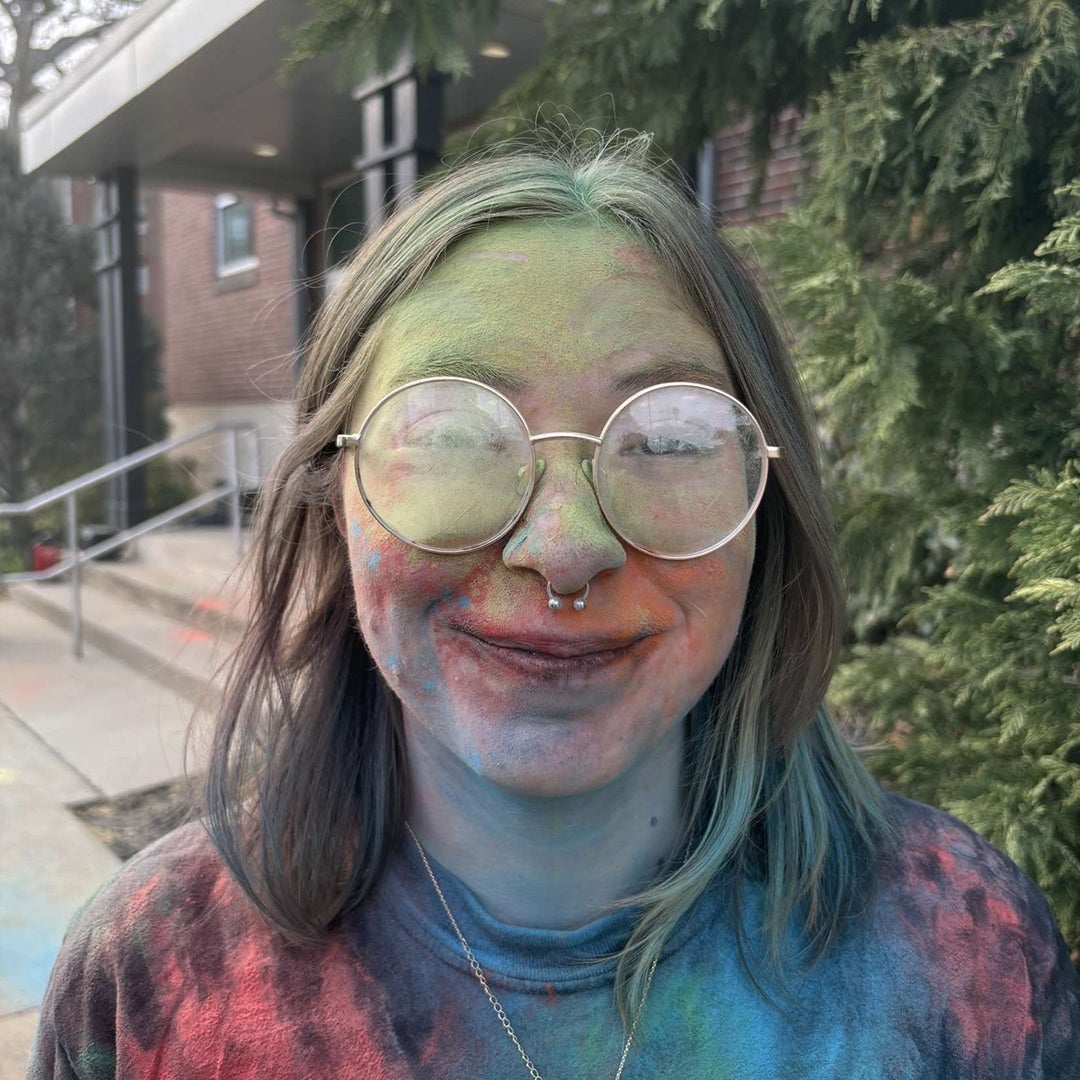 A student smiles at the camera while covered in colors from Marshall University's Herd Holi celebration