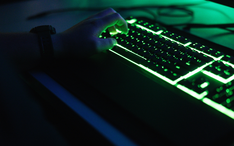 A hand types on a bright green, backlit keyboard