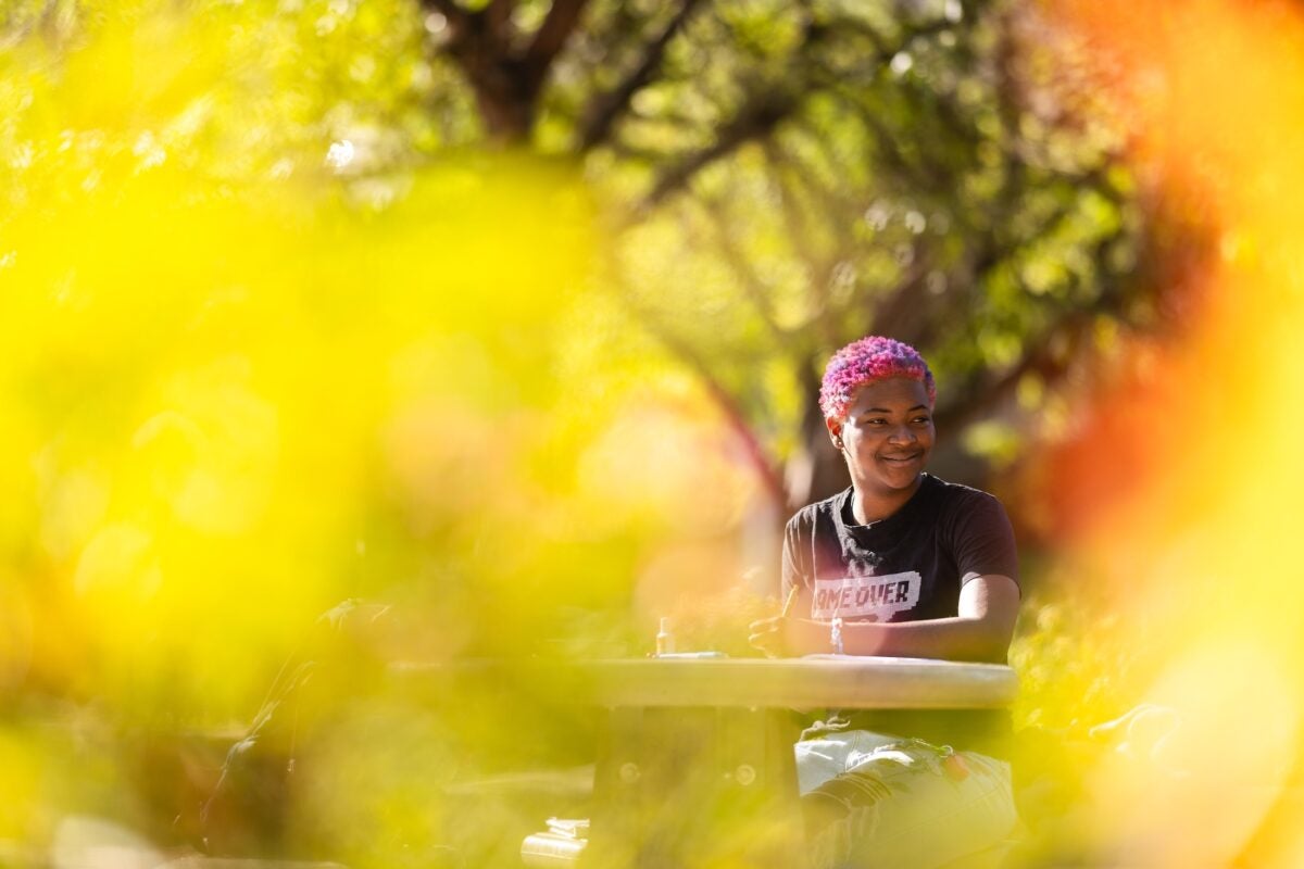 student sitting outside at a table with yellow leaves in the foreground
