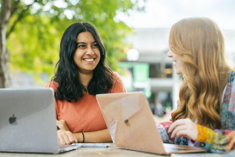 Students with laptops study together at a table outside